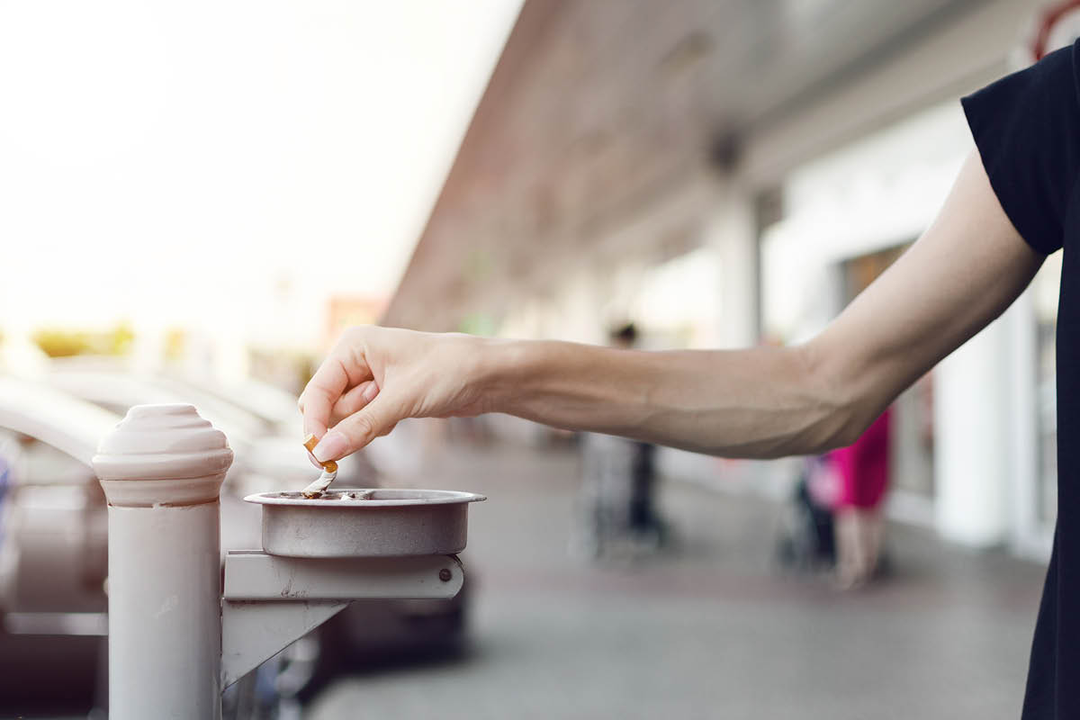 Arm putting out cigarette in an outdoor ashtray.