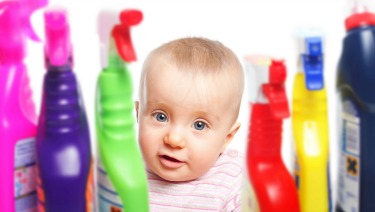 Baby surrounded by cleaning supply bottles.