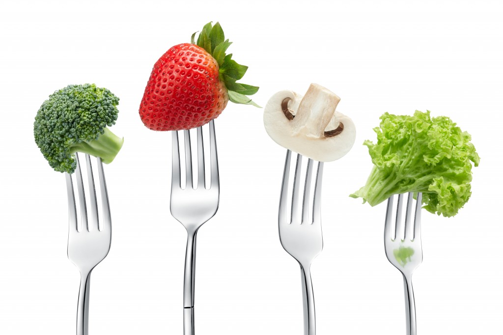 Four forks with broccoli, a strawberry, a mushroom and lettuce.